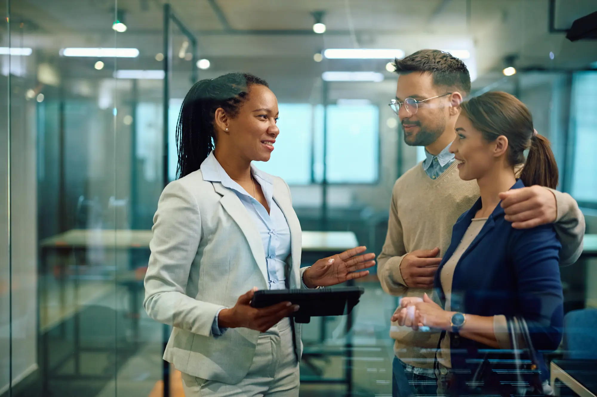 Happy black financial advisor using touchpad while talking to couple in office
